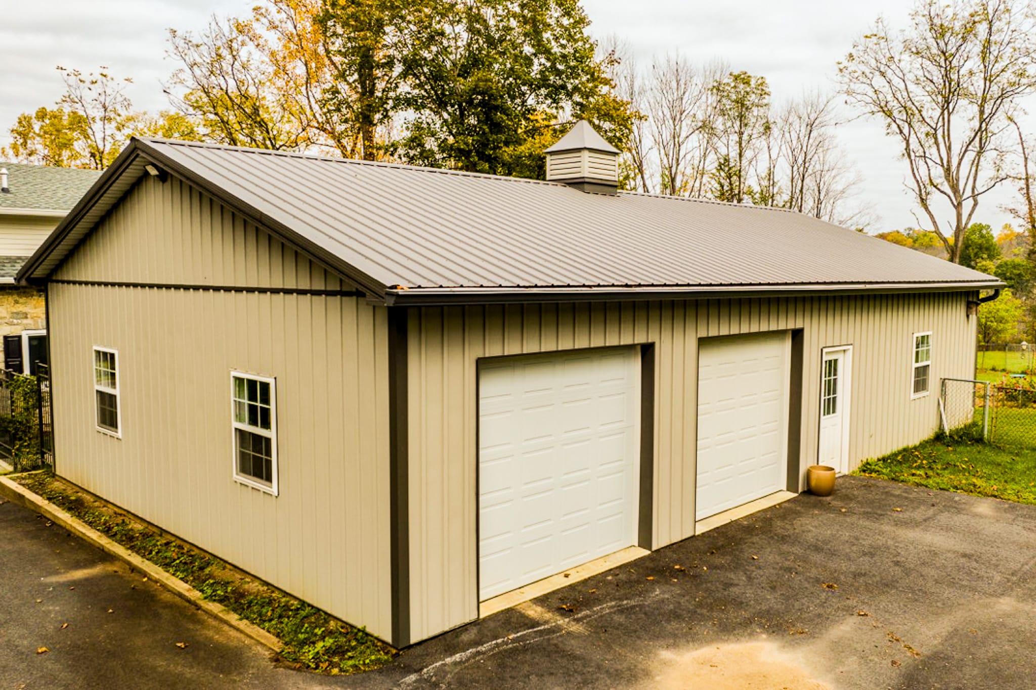 An example of our Metal Siding & Metal Roofing in Hammonton - A beige metal building with a gray metal roof and multiple white garage doors, surrounded by a paved driveway and trees in the background.